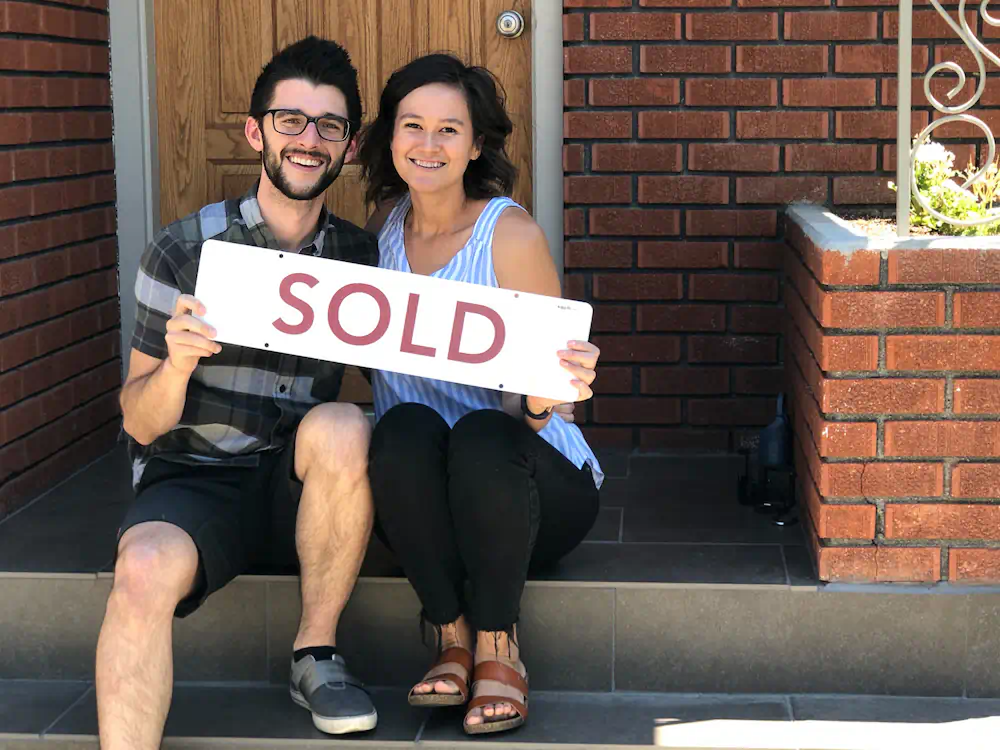 Charming couple with a sold sign, sitting on the porch of their updated mid-century ranch home on the Boise Bench.