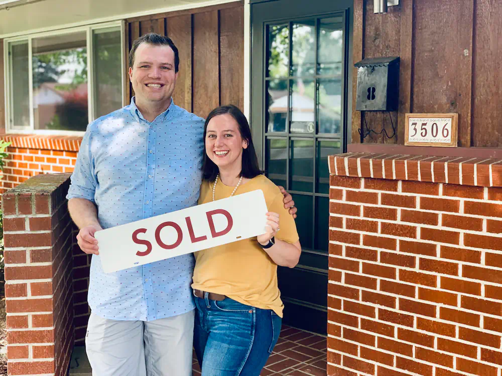 Happy first-time buyers with a sold sign in front of their mid-century ranch home on the West Bench.