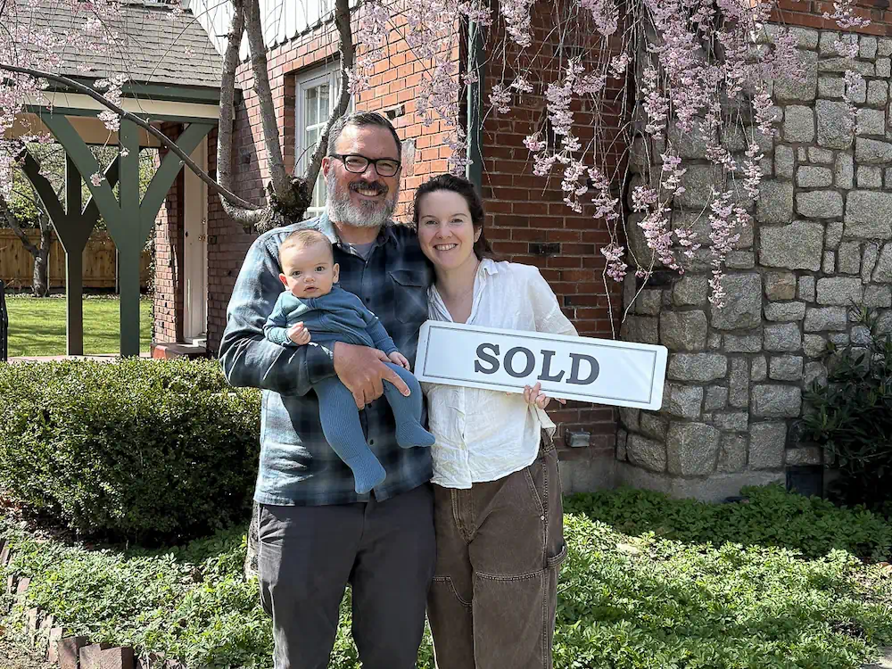 Happy first-time buyer clients Harry and Katherine celebrating in front of their Boise bench cottage with their new baby!