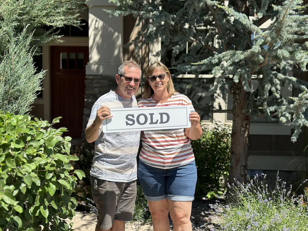Happy couple holding a sold sign in front of their new Eagle residence after relocating to the Treasure Valley.