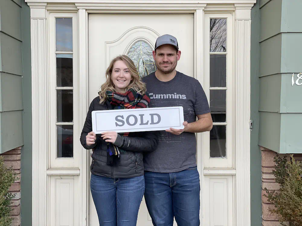 First-time buyers holding a sold sign in front of their West Bench home close to shopping and entertainment.