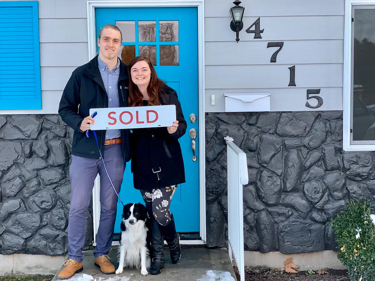 Smiling first-time home buyers, The Ruddy Family, holding a sold sign in front of their Boise Bench cottage with their new puppy!